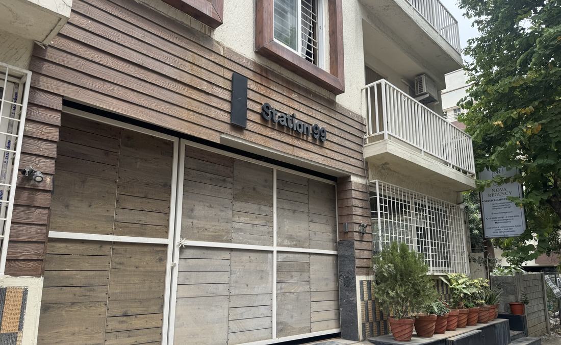 The Nova Regency street frontage on Ashwini Layout — timber-clad ground floor, the gate, a row of terracotta planters and the Nova Regency board