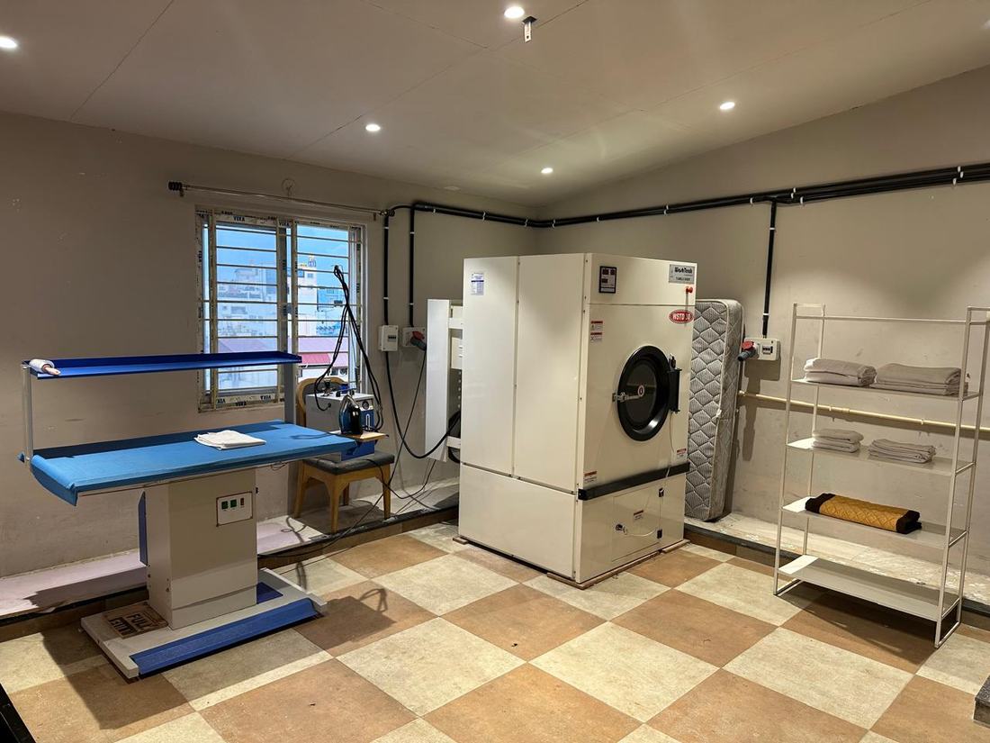 The seventh-floor linen room: a commercial tumble dryer, a vacuum ironing table with a steam iron, and shelves of folded linen