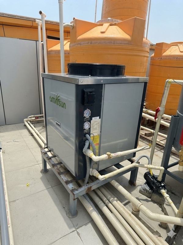 The rooftop heat pump with pressure gauges, standing in front of the building's overhead water tanks