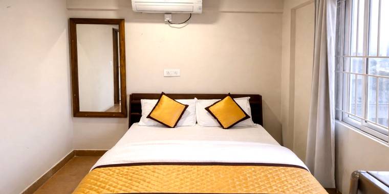 A made bed with a full-length mirror and daylight from two windows